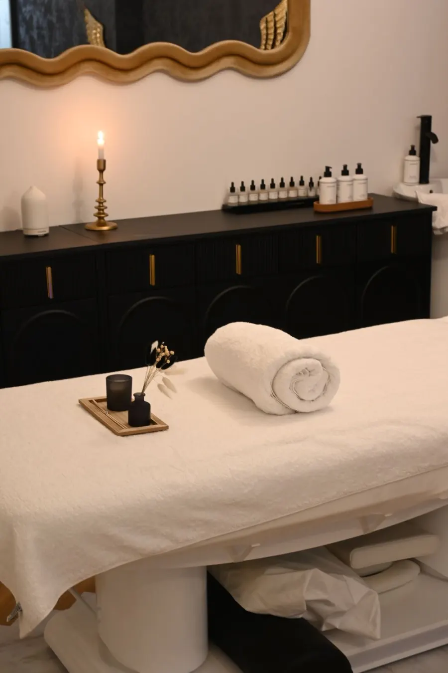 Massage table with rolled towel, candle and essential oils in a softly lit spa room